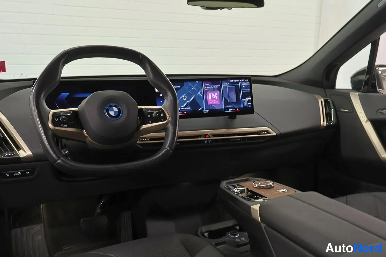 Etuviisto: Kuljettajan puolen näkymä: BMW-ohjauspyörä, laaja infotainment-näyttö keskikäytävä ja istuinosat.