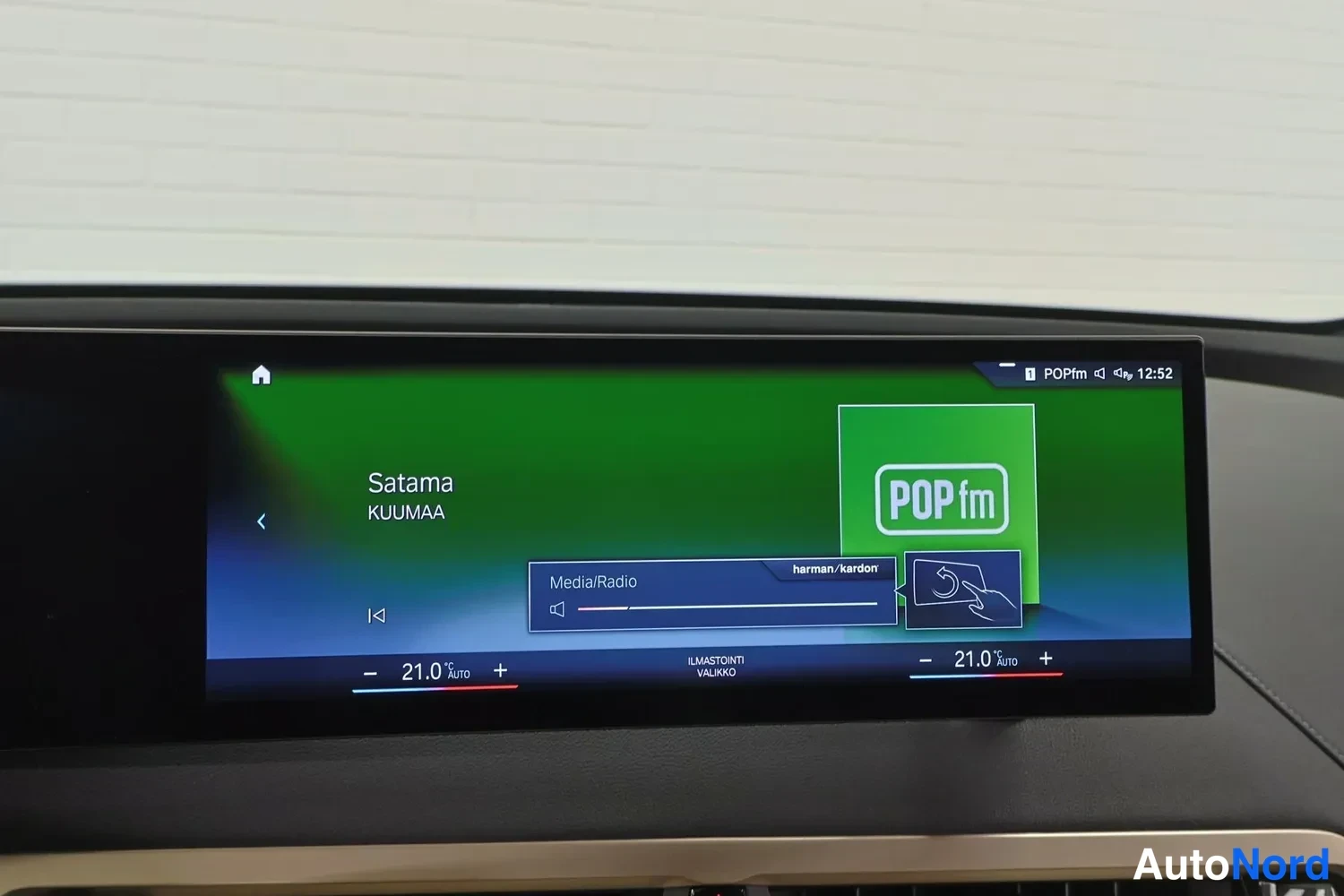 Yksityiskohta: Auton kojelaudan infotainment-näyttö, jossa toistuu POPfm-radio ja kappale Satama artistilta KUUMAA. Näytöllä näkyvät Media/Radio-valikko, harman/kardon-merkint