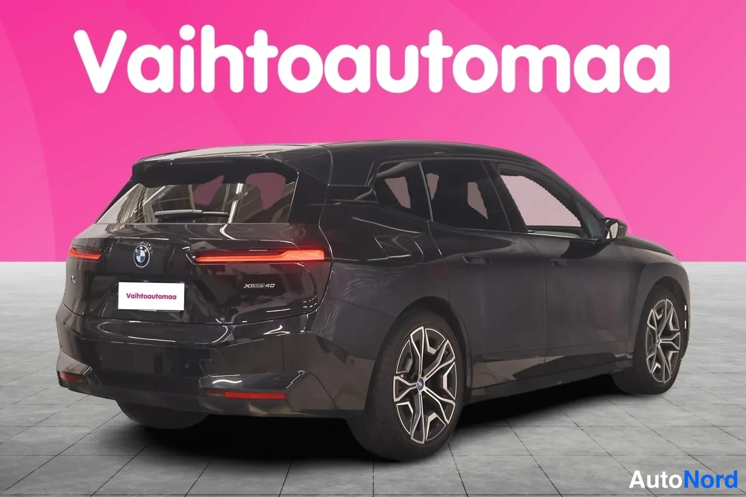 Takaviisto: Mustan BMW iX:n takakulmanäkymä, jossa näkyvät takavalot, avatava takaluukku ja kevytmetallivanteet.
