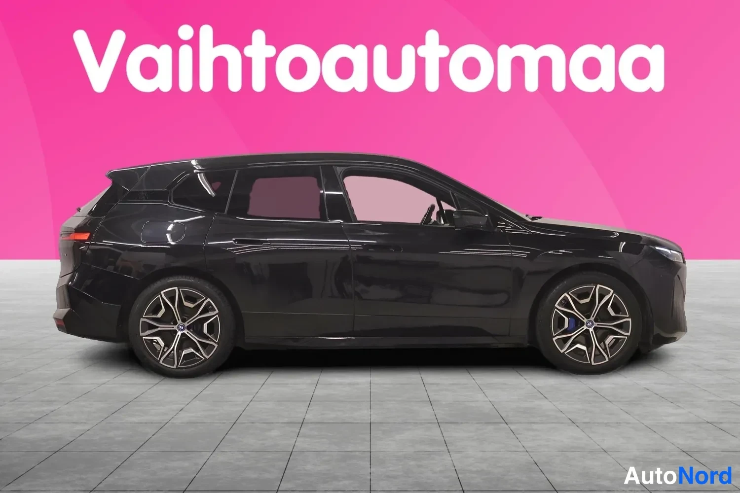 Etuviisto, nokka oikealle: Mustan BMW iX:n sivuprofiili, jossa näkyvät ovet, lasitettu panoraamakatto ja kevytmetallivanteet.