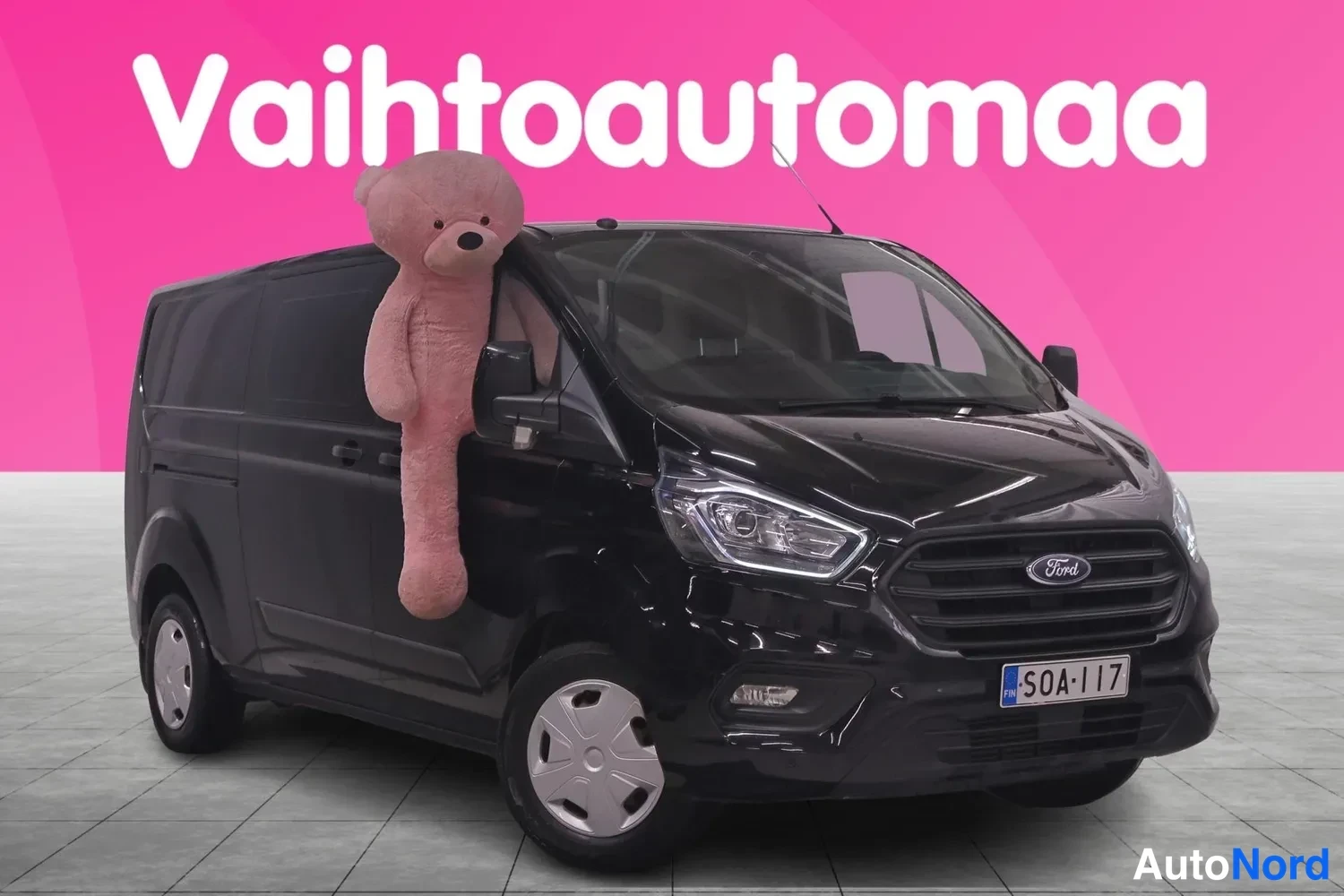 Etuviisto, nokka oikealle: Musta pakettiauto etu-3/4-kulmassa, keula oikealla; etusäleikössä Ford-merkki ja peiliin nojaa suuri pehmokarhu.