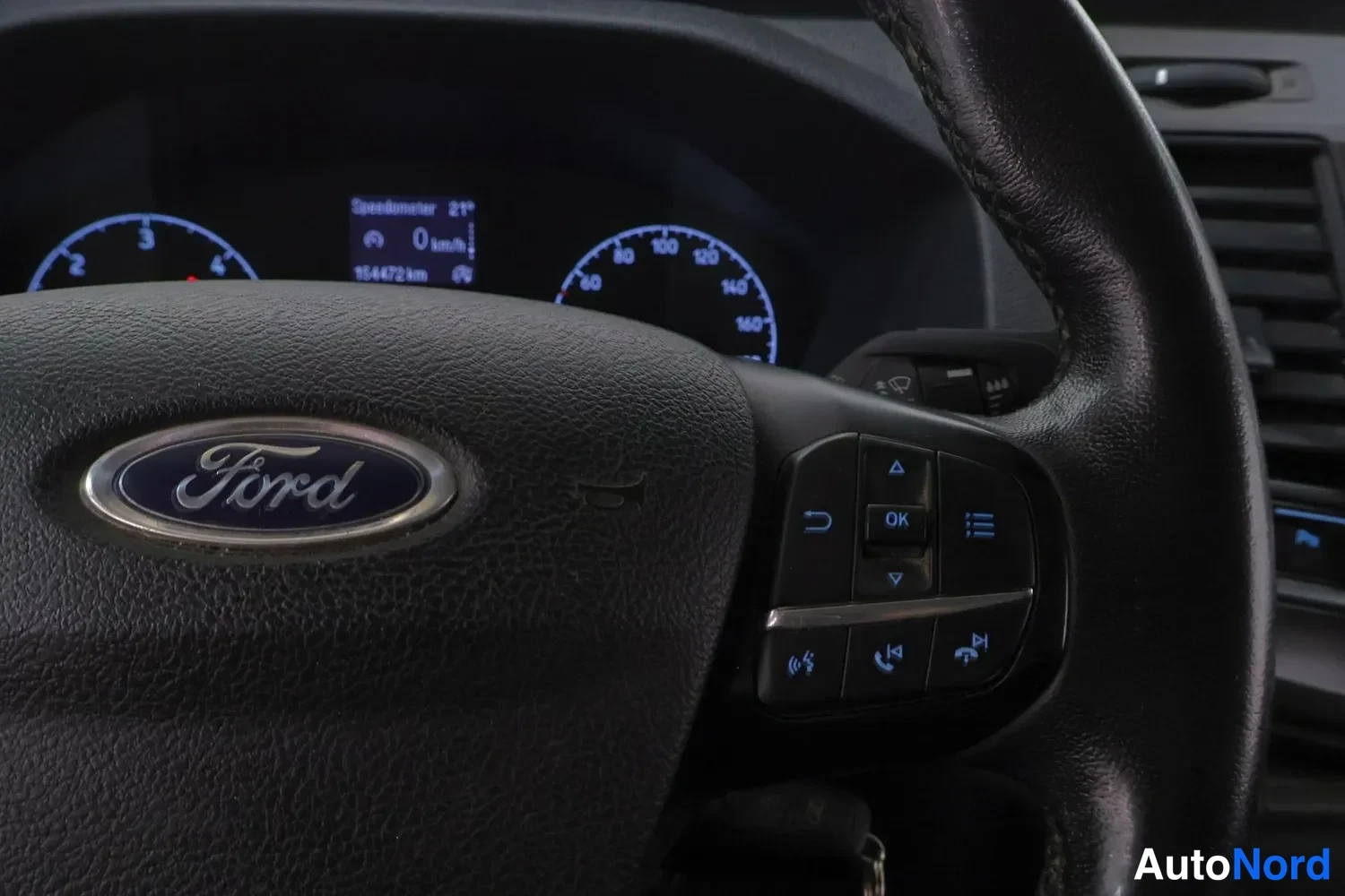 Yksityiskohta: Ohjauspyörän Ford-merkki ja kojelaudan mittarit, mittaristossa lukema 154472 km.