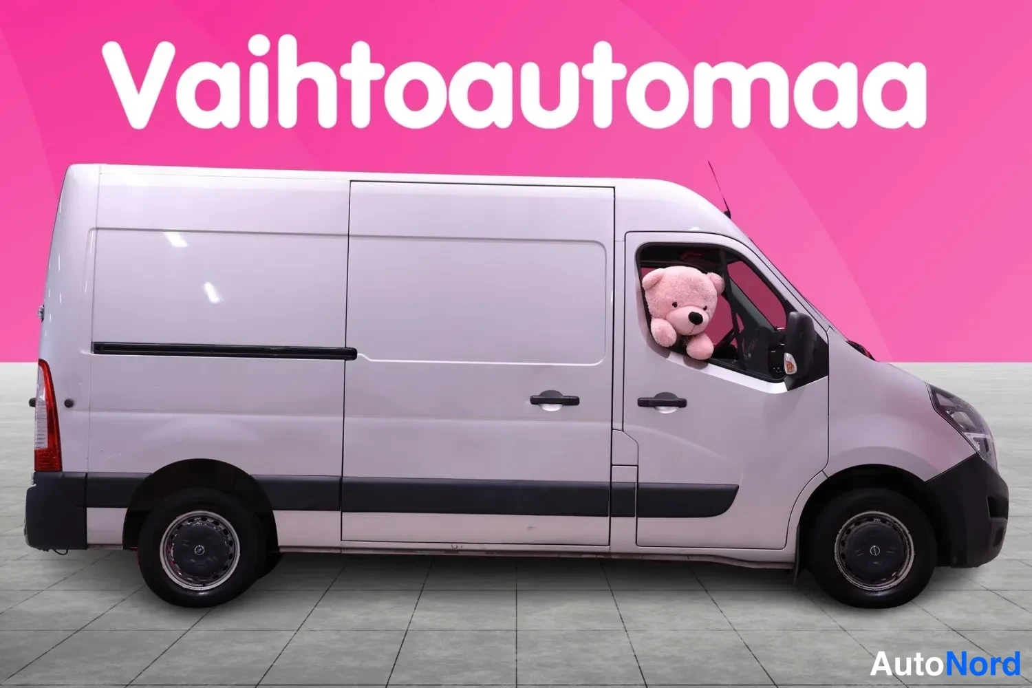 Sivulta: Valkoinen pakettiauto sivukuva vasemmalta, kuljettajan ikkunasta pilkistää pehmolelu