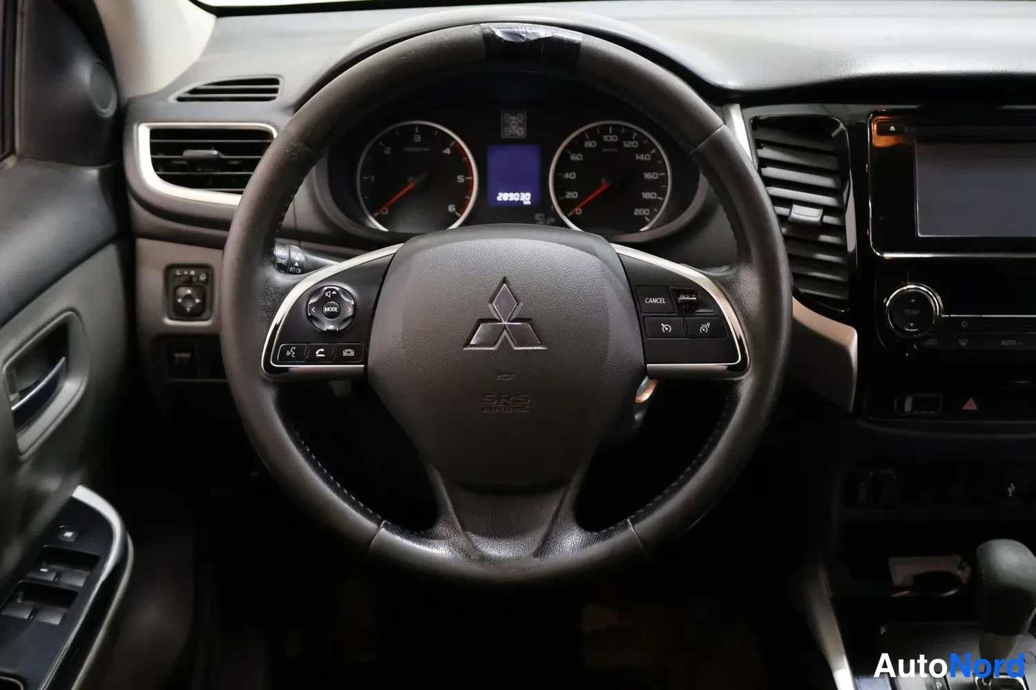 Sivulta: Ohjauspyörän lähikuva: Mitsubishi-tunnus, mittaristo, multifunktionapit ja kosketusnäyttö radio-osan yhteydessä.