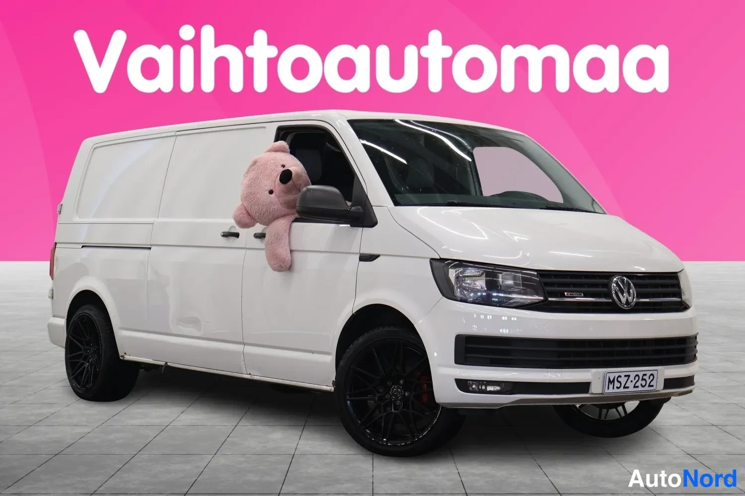Etuviisto, nokka oikealle: Valkoinen Volkswagen Transporter -pakettiauto kolmanneltakin sivulta, keula oikealla; mustat kevytmetallivanteet, rekisteri.