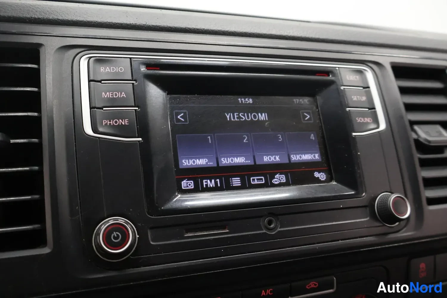 Muu: Lähikuva auton kojelaudan radioyksiköstä: näytöllä radioasema YLESUOMI, kello 11:58, lämpötila 17,5°C, FM1-taajuusalue ja esivalinnat 1–4. Painikkeita RADIO, ME