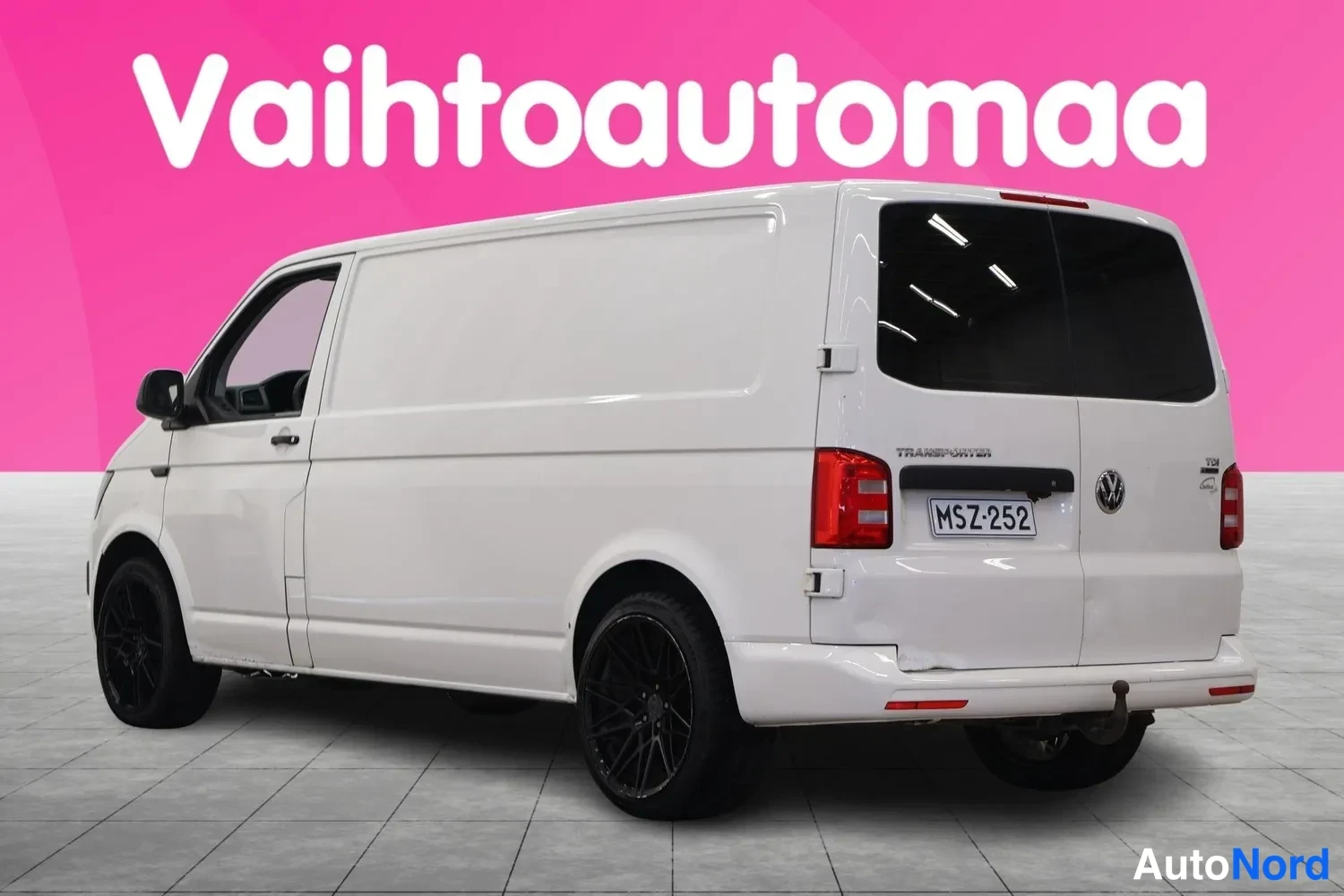 Takaviisto: Valkoinen pakettiauto takaa-vinosti, rekisteritunnus, mustat renkaat ja perävaunukytkin.