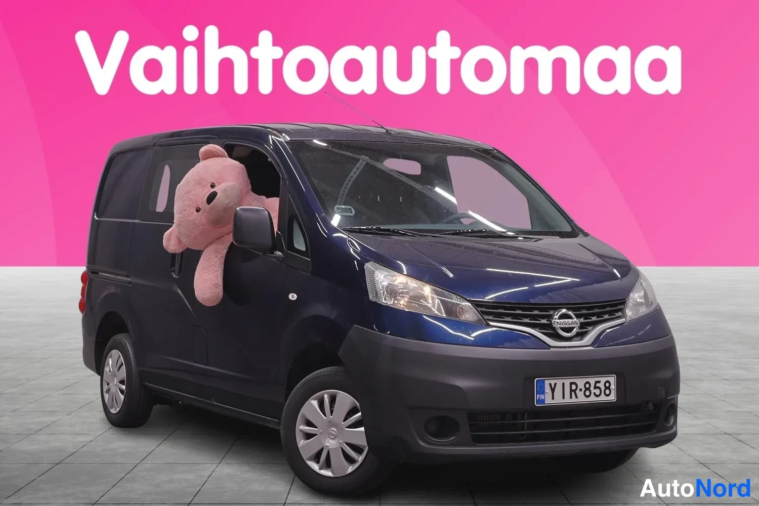 Etuviisto, nokka oikealle: Tummansininen Nissan NV200 -pakettiauto kolmesivukulmassa, keulakilpi ja moottoritien tunniste näkyvät, rekisteritunnus.