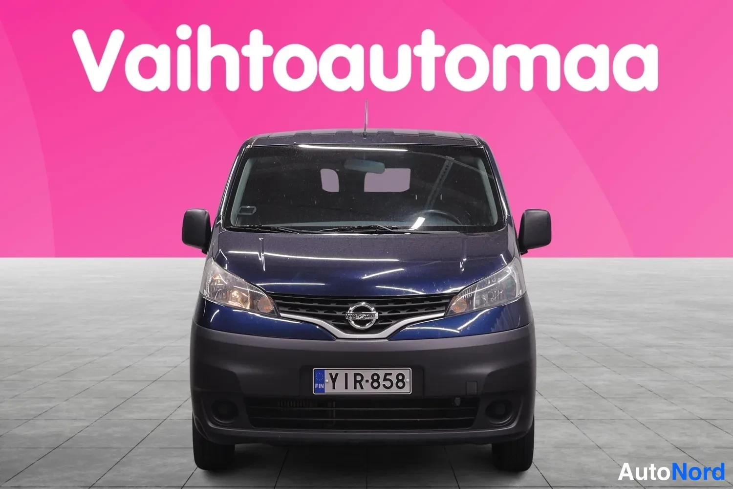 Edestä: Nissan NV200 -pakettiauto suoraan edestä, rekisteritunnus, keulakilpi ja takamoottoritunnus näkyvät.