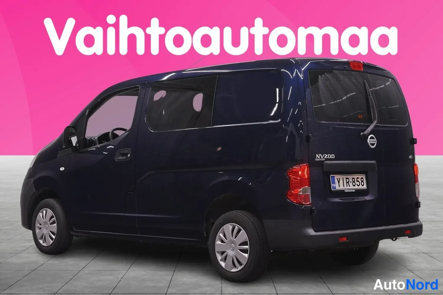 Takaviisto: Tummansinisen Nissan NV200 -pakettiauton takanurkkakuva, rekisterikilpi ja NV200-merkintä peräovessa.