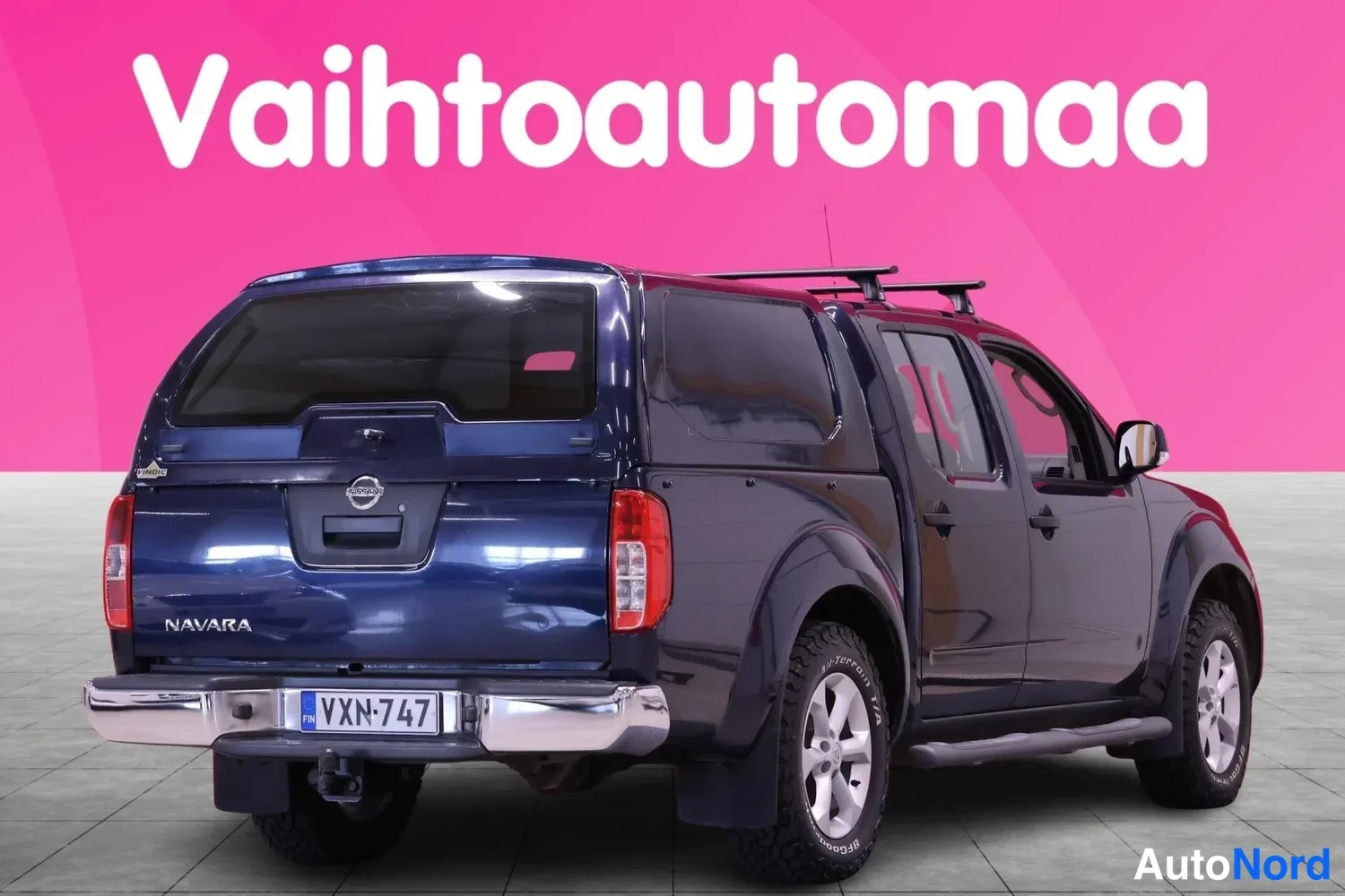 Takaviisto: Tummansininen Nissan Navara-noutoauto takakulmasta oikealta, NAVARA-kylkiteksti ja rekisterikilpi V XN-747.