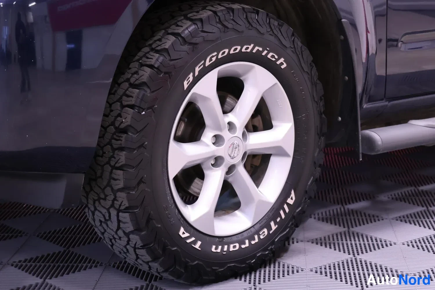 Sivulta: Sinisen auton etupyörän lähikuva: hopea viisipuinen kevytmetallivanne ja BFGoodrich All-Terrain T/A -nastaton maastorengas.