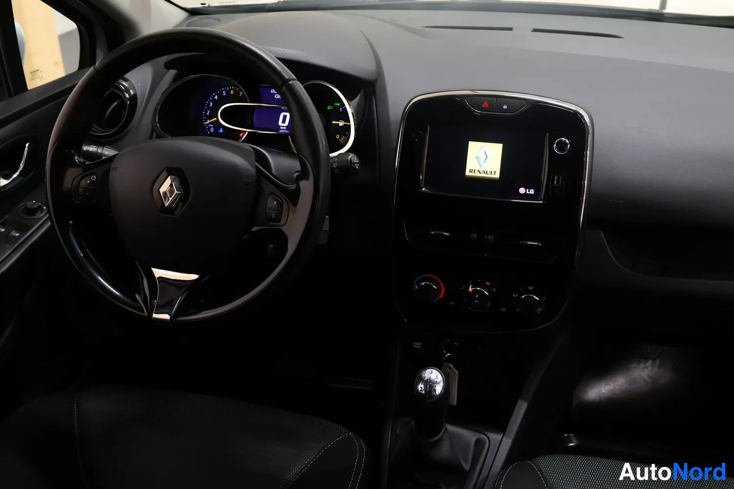 Muu: Renaultin ohjaamon yleiskuva: ohjauspyörä, mittaristo, Renault-tunnus näytöllä ja manuaalivaihdekeksi.