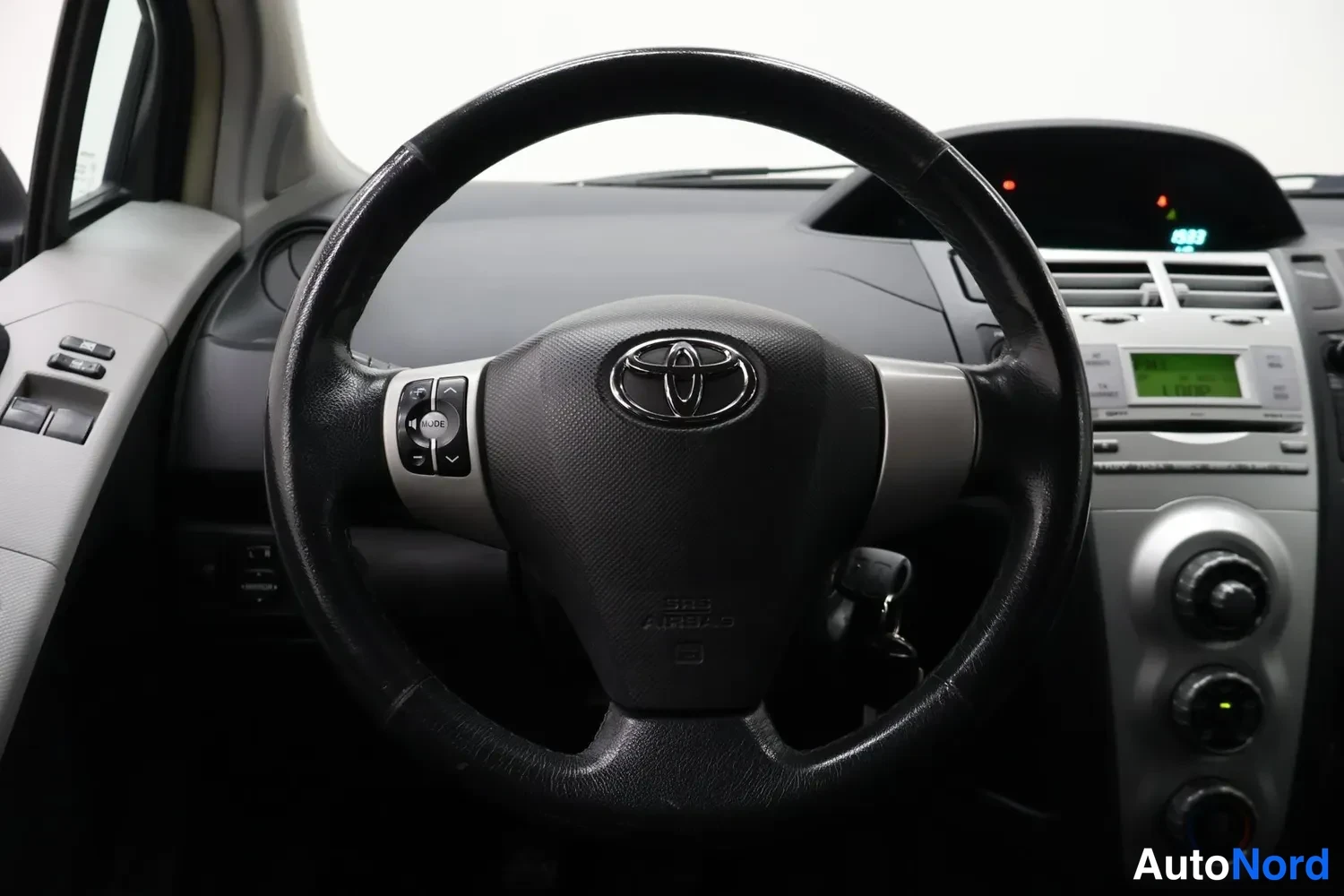 Muu: Ohjauspyörän näkymä edestä, keskellä Toyota-merkki ja monitoiminapit, taustalla radio ja ilmastointisäätimet.