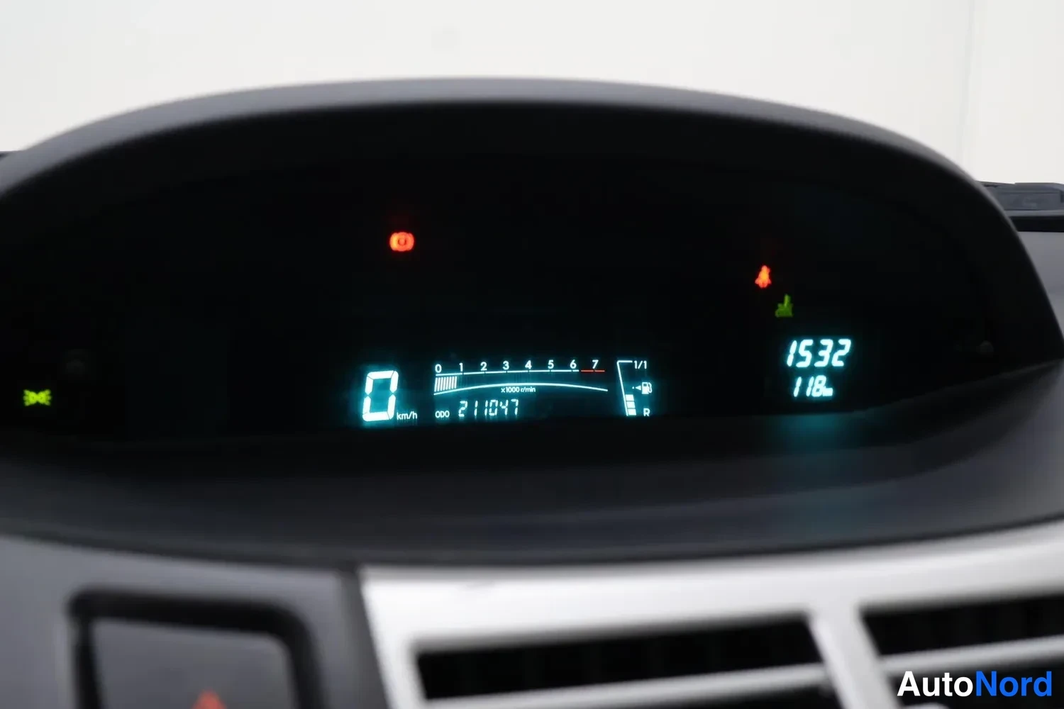 Yksityiskohta: Lähikuva tummasta digitaalisesta mittaristosta, jossa lukema 0 km/h, kokonaiskilometrimäärä 211047, polttoaineneula, kellonaika 15:32 ja pieni matkamittari 11,8