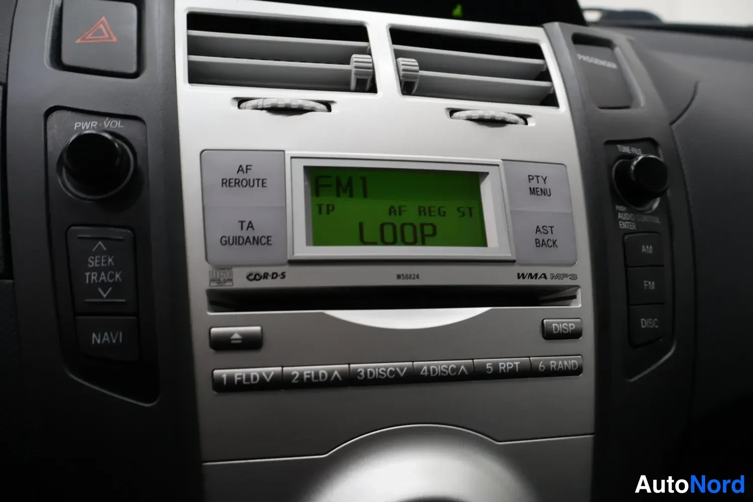 Yksityiskohta: Lähikuva keskikonsolin hopeanharmaasta radiopaneelista, jonka näytössä lukee FM1, TP, AF REG ST ja LOOP, ja jossa on CD-S-merkintä, WMA MP3 -tuki, NAVI-, DISP-