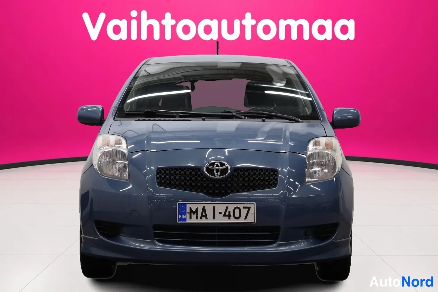 Edestä: Sininen Toyota Yaris -henkilöauto suoraan edestä, rekisteritunnus.
