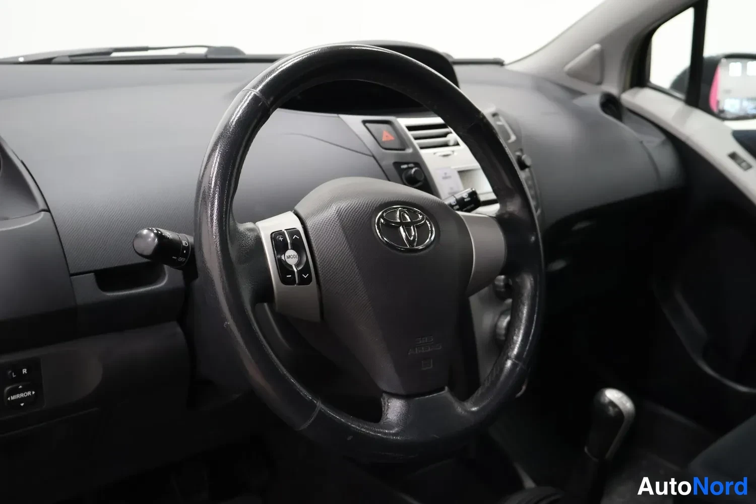 Muu: Ohjauspyörän lähikuva Toyota-merkillä ja monitoiminapeilla kojelaudan taustalla.