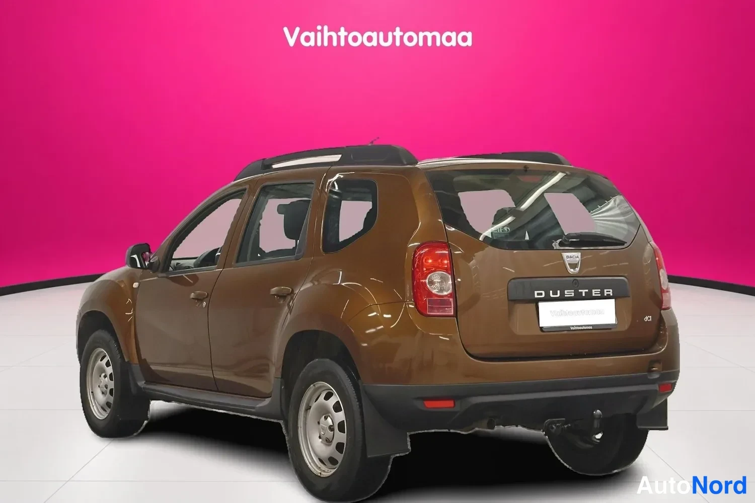 Takaviisto: Ruskea Dacia Duster takaa vasemmalta, perä ja DUSTER-merkintä näkyvissä.