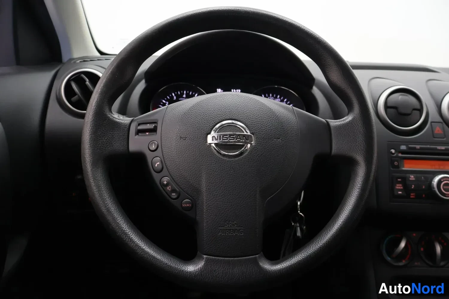 Muu: Nissan-ohjauspyörä lähikuvassa, mittarit ja radio paneli taustalla.