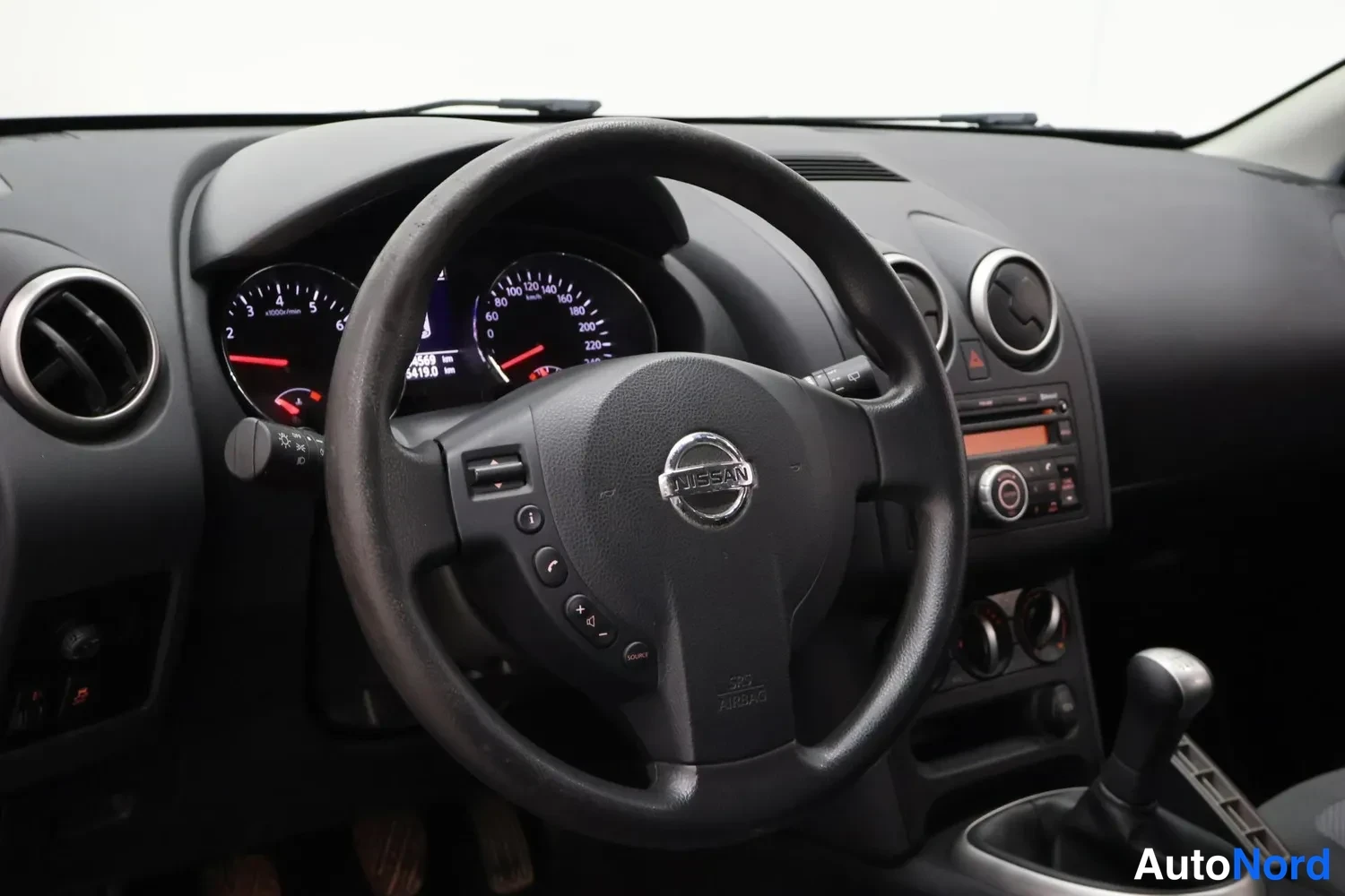 Muu: Ohjaamo Nissan-merkkisellä ohjauspyörällä, mittarit ja manuaalivaihtoehdeisto näkyvät.