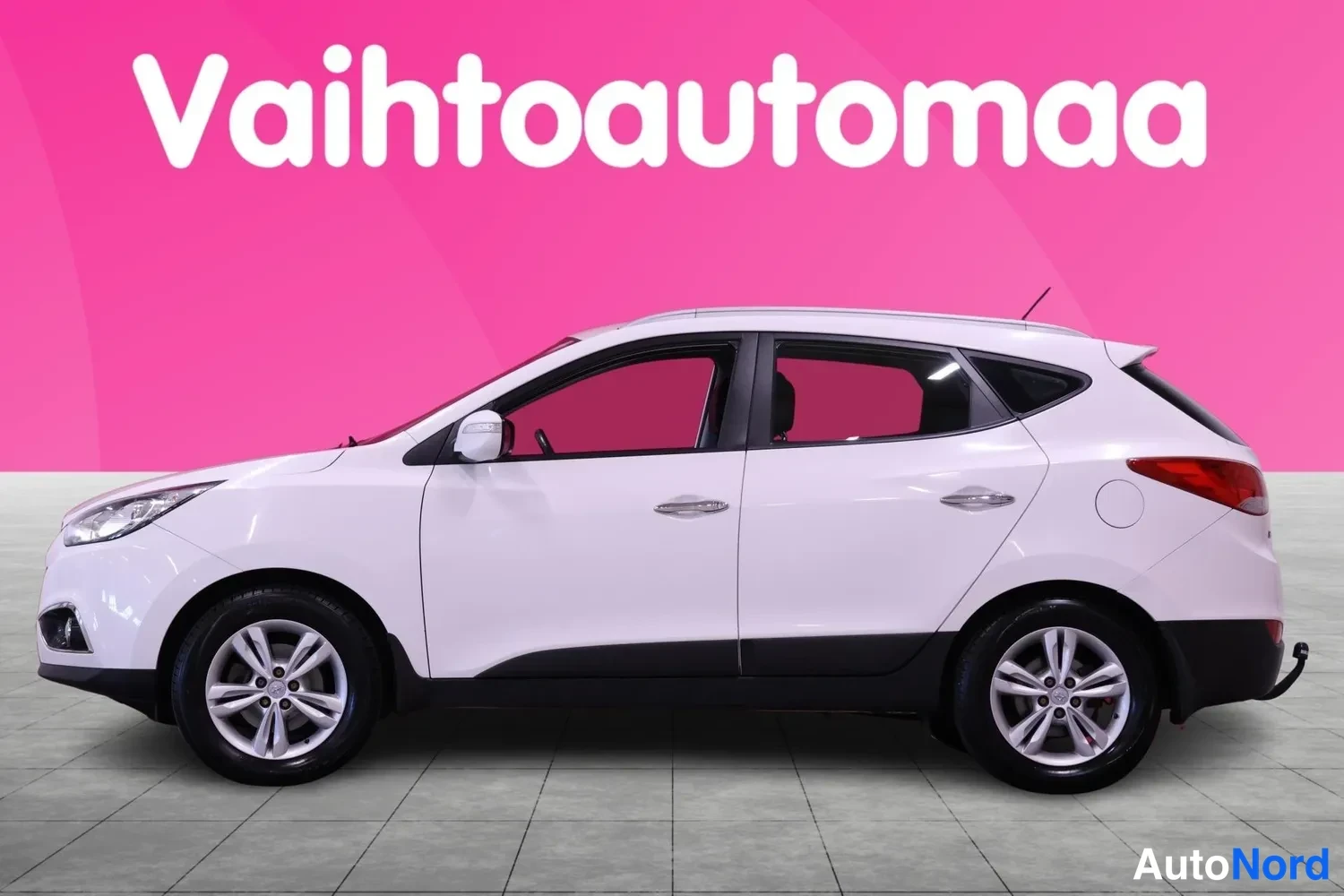 Sivulta: Valkoinen Hyundain kattopaikkamallinen auto, profiilikuvassa oikea sivu. Alumiini-vanteet, mustat korvakorut ja katonraide näkyvät.