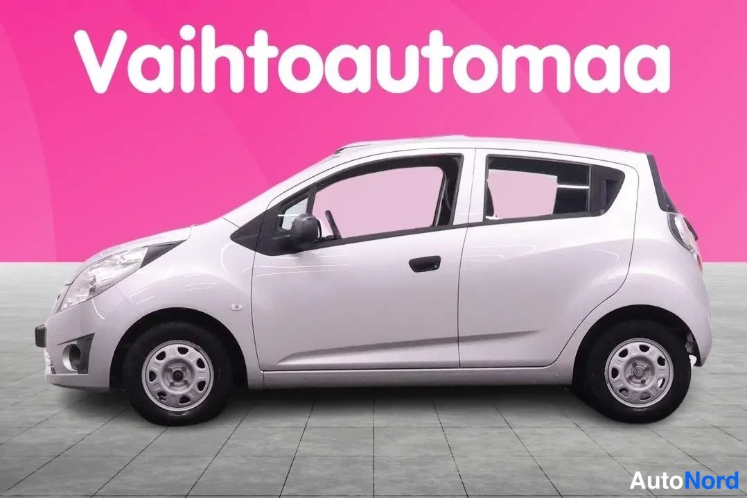 Etuviisto, nokka vasemmalle: Hopeanvalkoinen Chevrolet Spark -henkilöauto sivulta, molemmat sivuovet ja pyörät näkyvät.