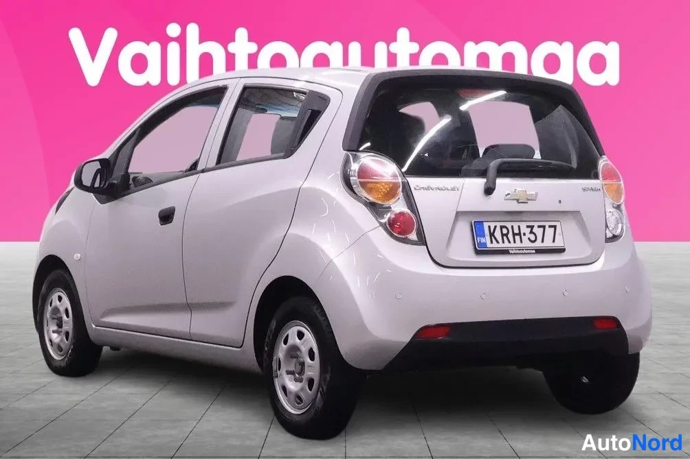 Takaviisto: Hopeanvalkoinen Chevrolet Spark -henkilöauto takalenäkulmasta, takaovet ja takavalot näkyvät, rekisterikilpi.