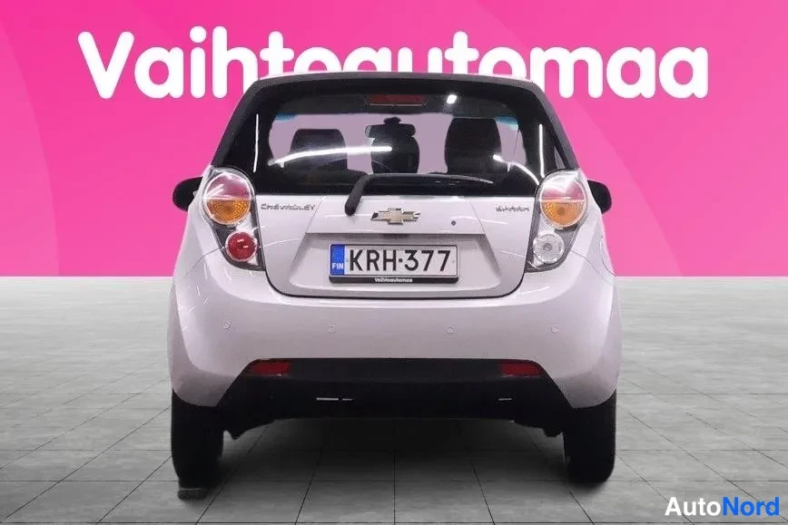Takaa: Hopeanvalkoinen Chevrolet Spark -henkilöauto suoraan takaa, takavalot, takiluukku ja rekisterikilpi näkyvät.