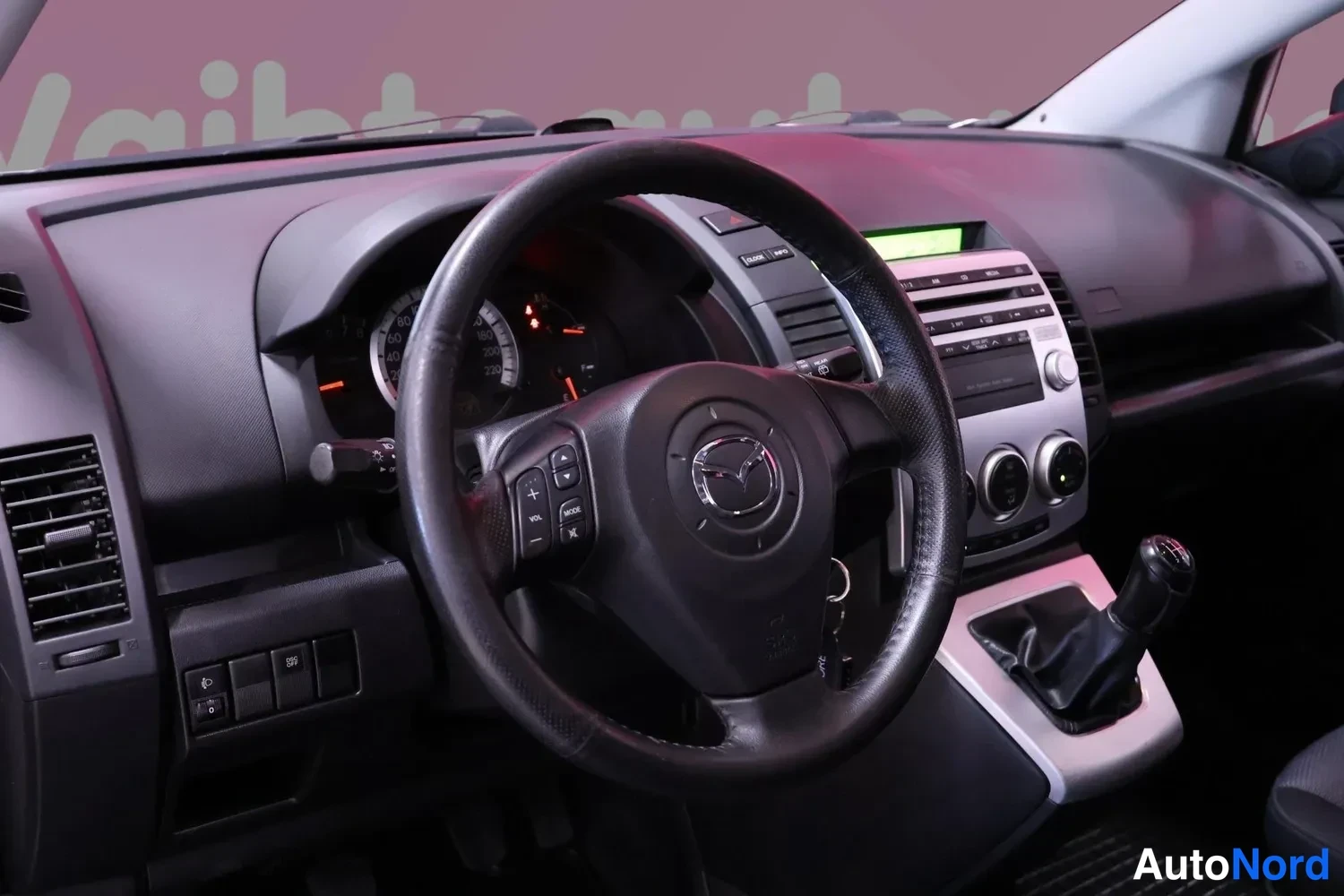 Muu: Ohjaamo vasemmalta: Mazda-ohjauspyörä, manuaalivaihteiston vaihdekeila ja keskikonsolin radio, kojelaudan näyttö vihreä.