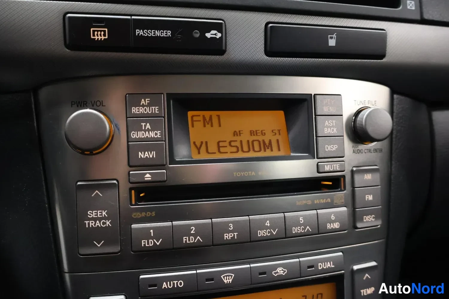 Yksityiskohta: Autoradion ja kojelaudan ominaisuuspainikkeiden lähikuva; näytöllä FM1 ja teksti AF REG ST YLESUOMI, painikkeissa muun muassa AF REROUTE, TA GUIDANCE, NAVI ja M