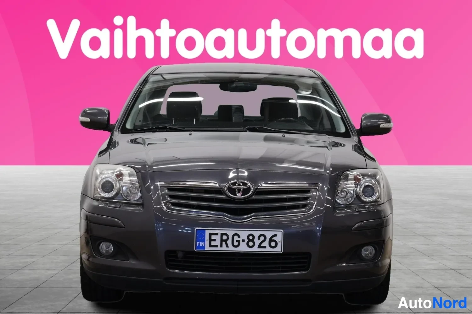 Edestä: Tummanharmaan sedanin etuosasta suoraan edestä, Toyota-merkki ja rekisterikilpi.