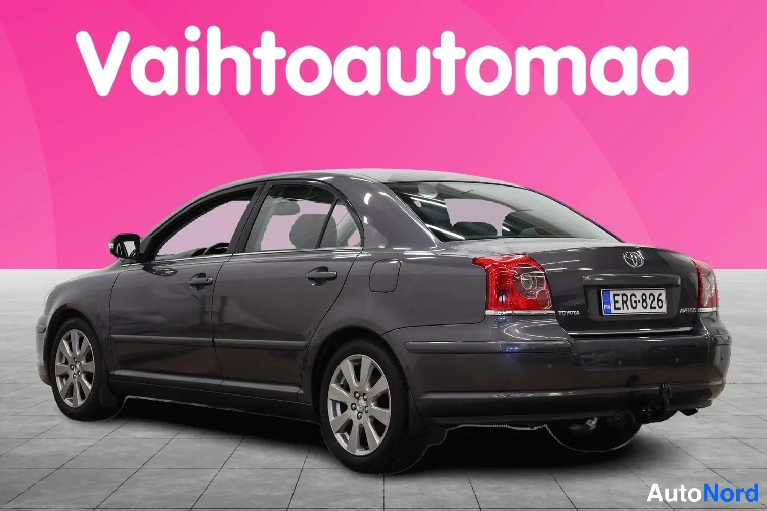 Takaviisto: Tummanharmaa Toyota Avensis -sedan takaa sivusta kuvattuna, rekisteritunnus.