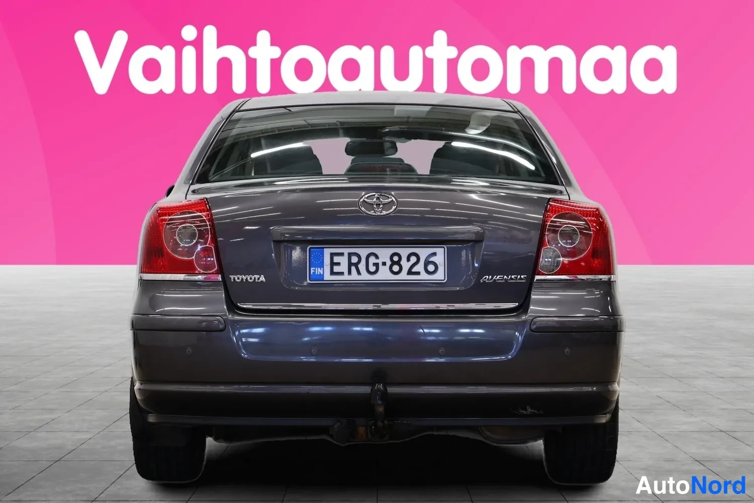 Takaa: Tummanharmaan Toyota Avensin perä suoraan takaa, rekisteritunnus ja hinauskoukku.
