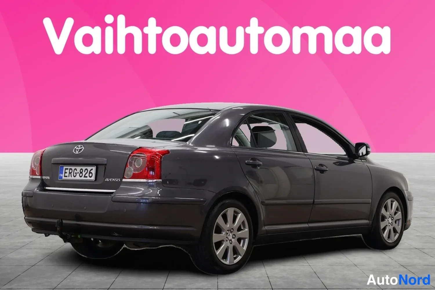 Takaviisto: Tummanharmaa Toyota Avensis -sedan takaa toisesta kulmasta, rekisteritunnus.