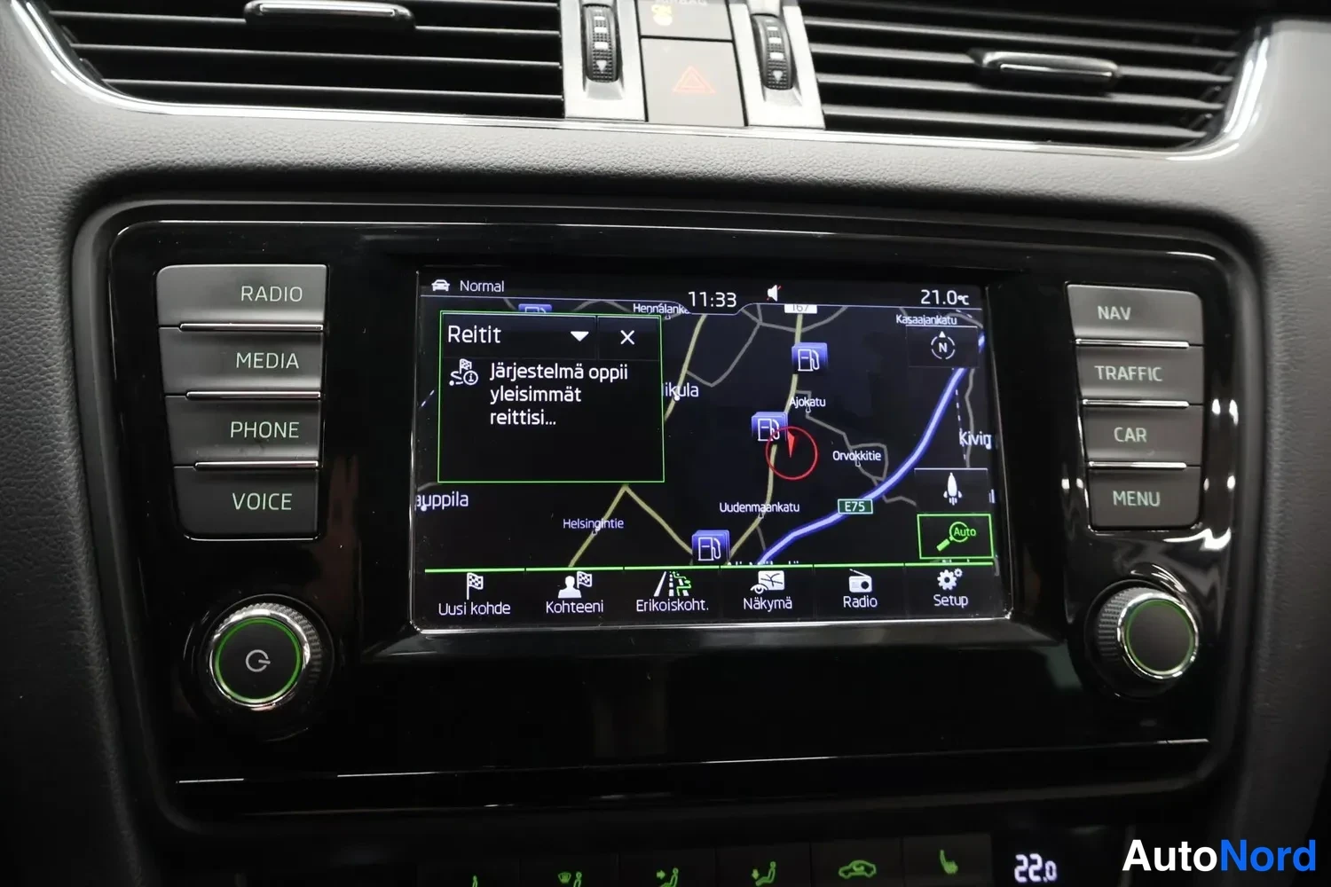 Yksityiskohta: Viihdejärjestelmän näyttö karttanavigoinnissa Reitit-valikolla; paneelissa painikkeet RADIO, MEDIA, PHONE, VOICE, NAV, TRAFFIC, CAR, MENU.