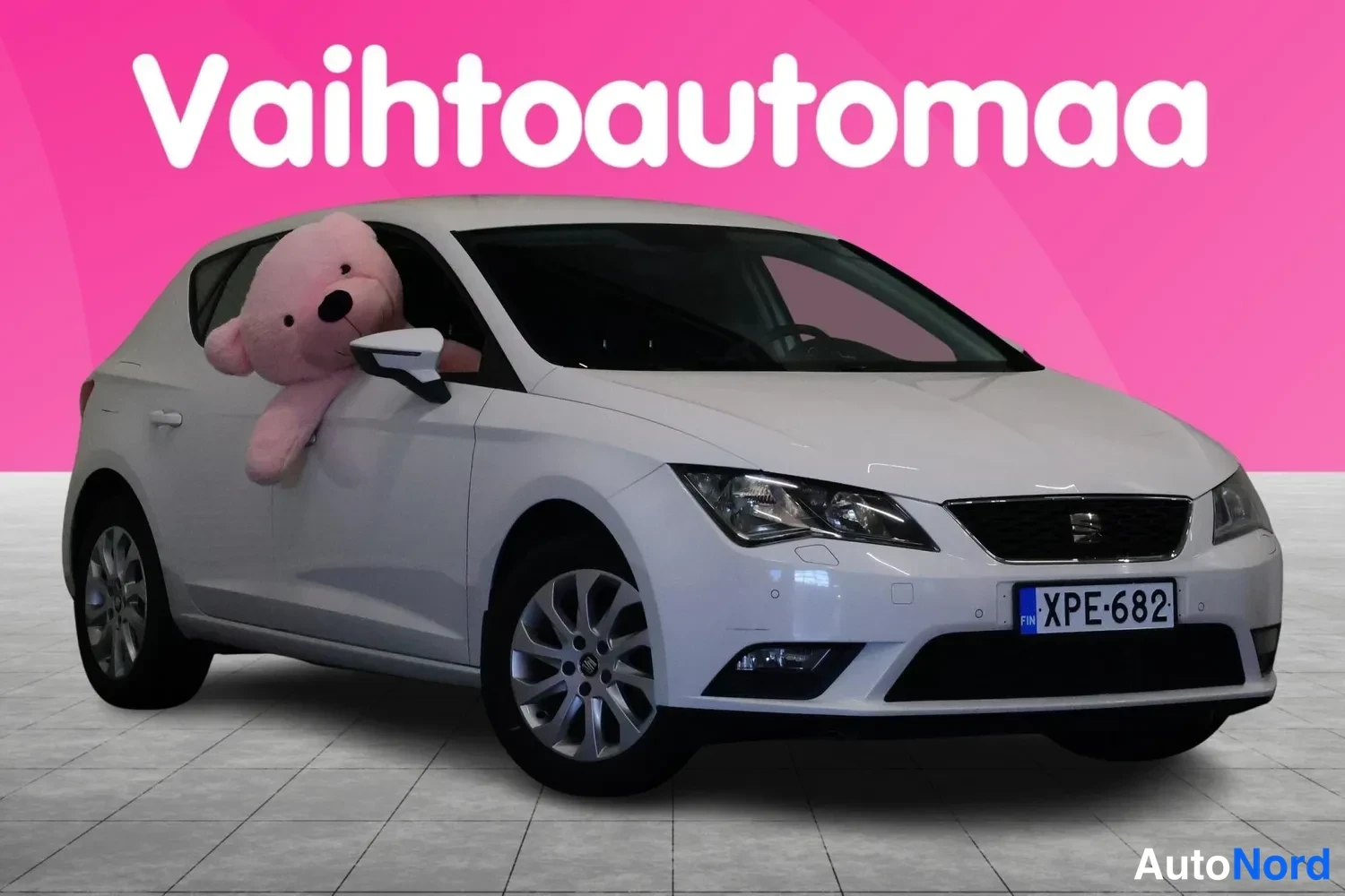 Etuviisto, nokka oikealle: Valkoinen Seat Leon farmariedustusauto etu kolmannesvasemmalla kuvakulmassa, rekisteritunnus, kuvattuna studio-tyyppisessä tilassa.