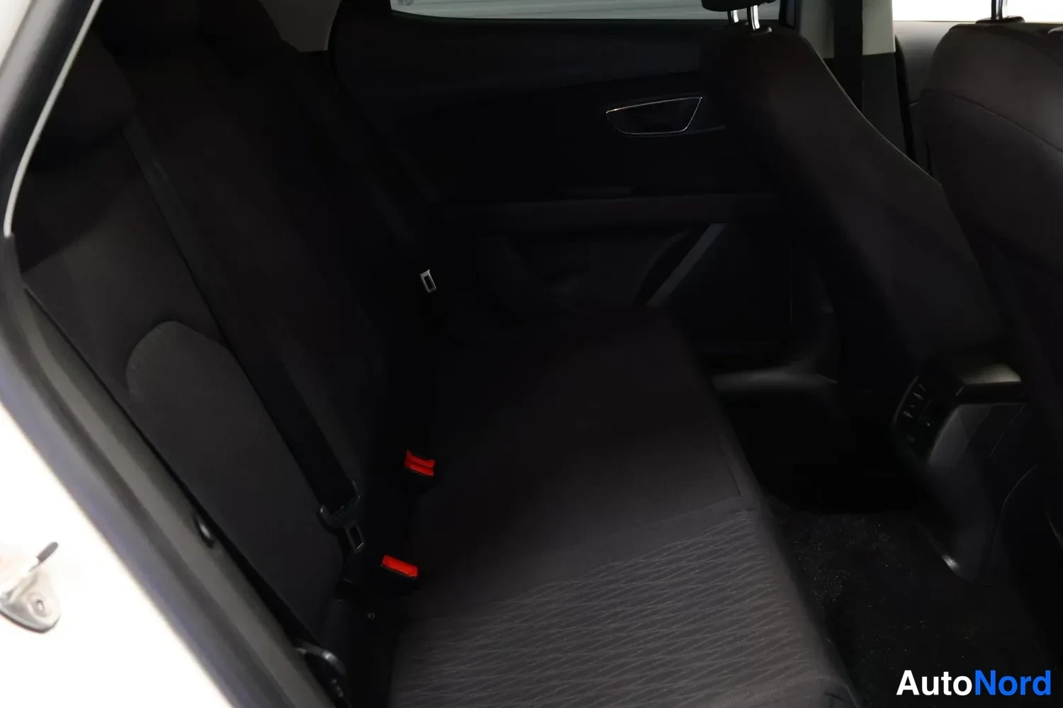 Muu: Seat Leonin takapenkin tumma sisätila heikossa valossa, turvavyönsoljet ja ovenkahvan metallikoriste näkyvissä.