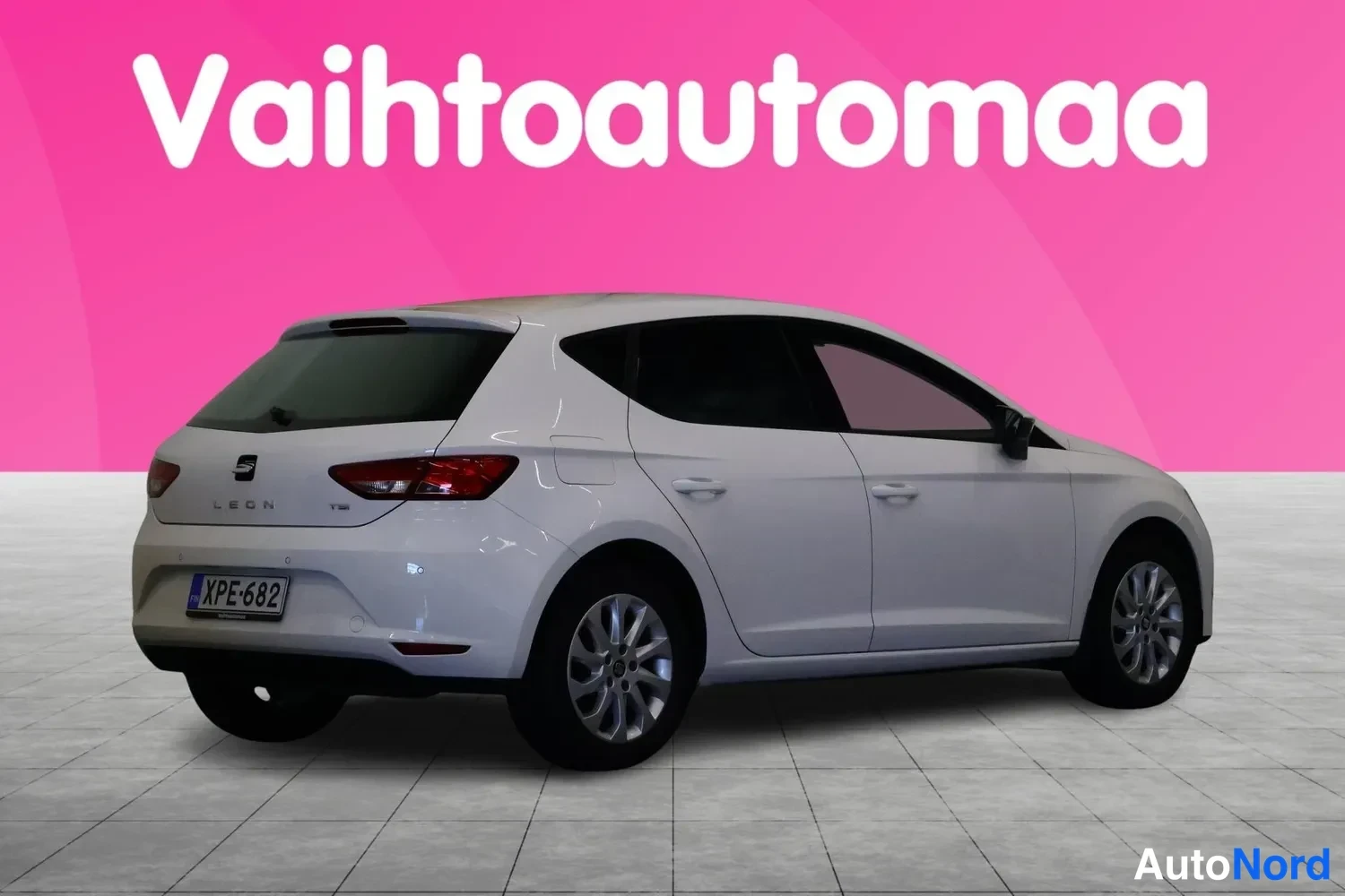 Takaviisto: Valkoinen Seat Leon -henkilöauto kuvattu takaa-vinosti studio­maisella pinkillä taustalla; rekisterikilpi näkyvissä.