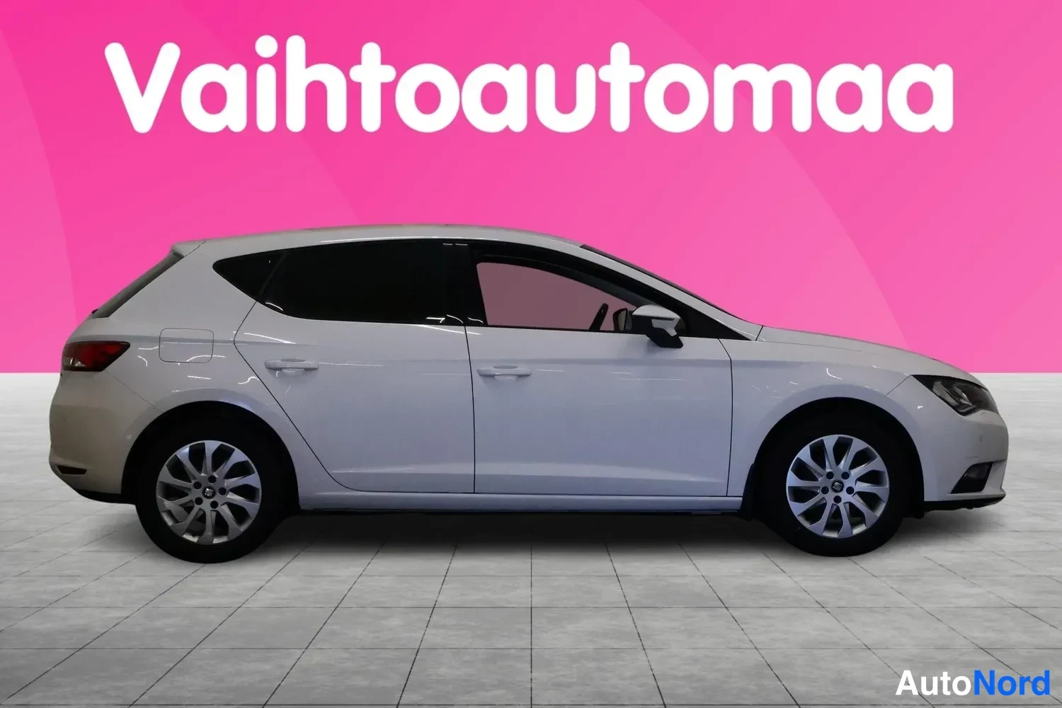 Etuviisto, nokka oikealle: Valkoinen Seat Leon -henkilöauto sivulta-vinosti etuosa oikealla, viisi ovea ja kolme sivuikkunaa näkyvissä.