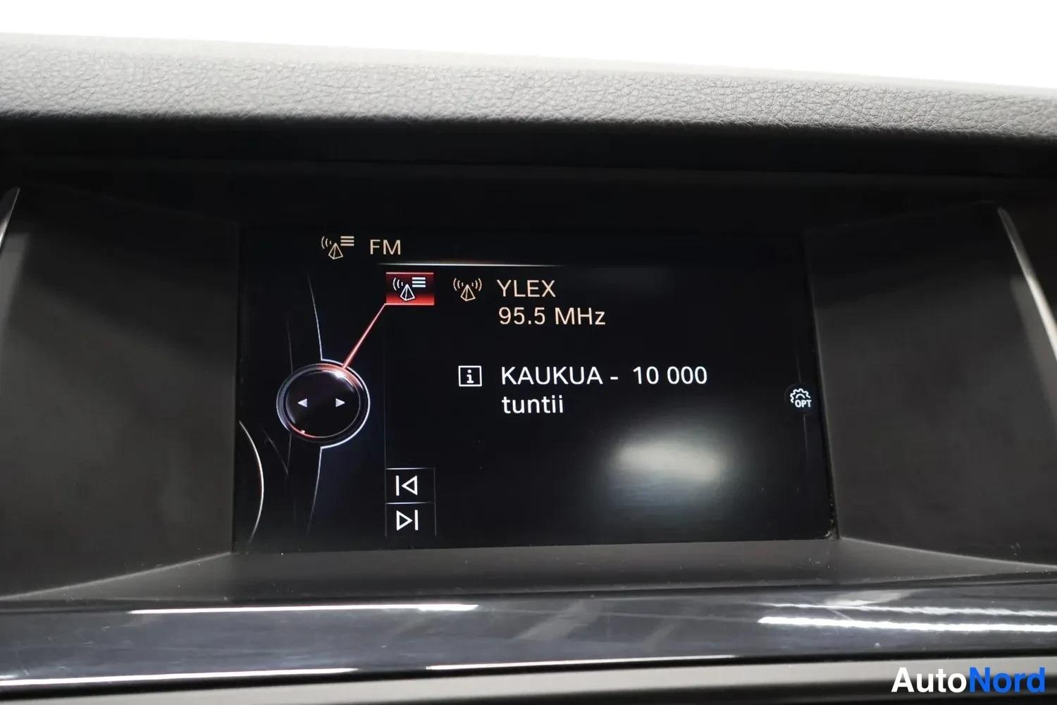 Muu: Auton kojelaudan näyttö, jossa FM-radio kanavalla YLEX 95.5 MHz ja teksti 'KAUKUA - 10 000 tuntii'.