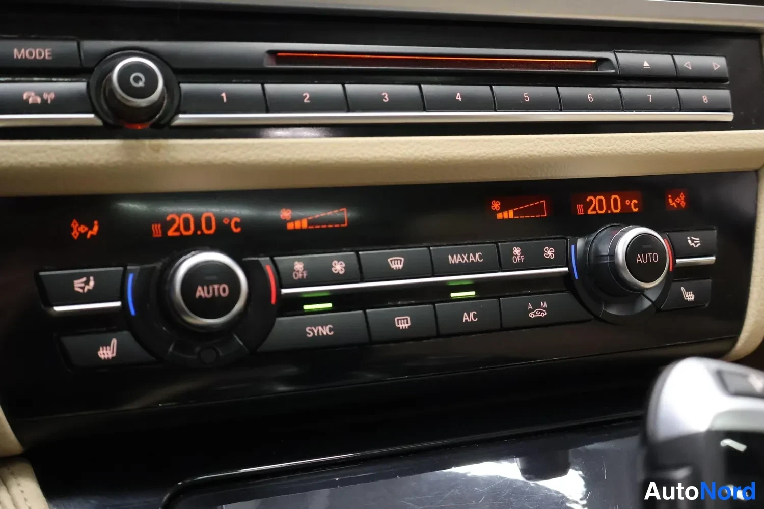 Muu: Lähikuva ilmastointipaneelista, näytöissä 20,0 °C, AUTO-säätörullat ja napit SYNC, A/C, MAX A/C sekä istuttimen toiminnot.