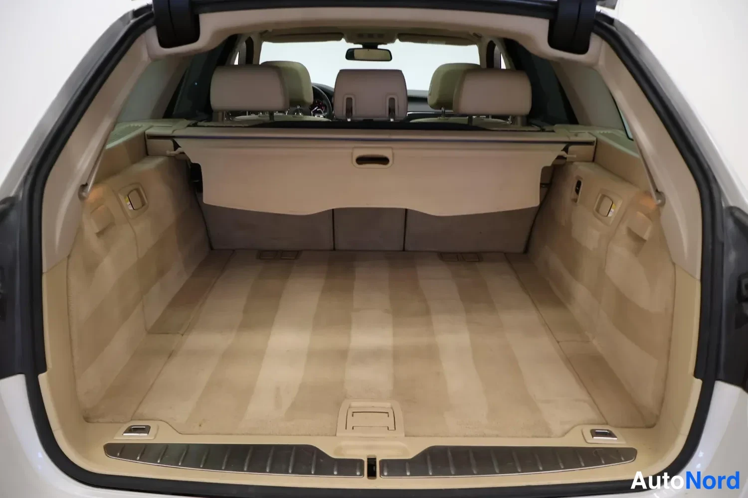 Tavaratila: View of the car's open trunk area showing beige carpeting on the floor and sides, along with the same beige cargo cover installed above.