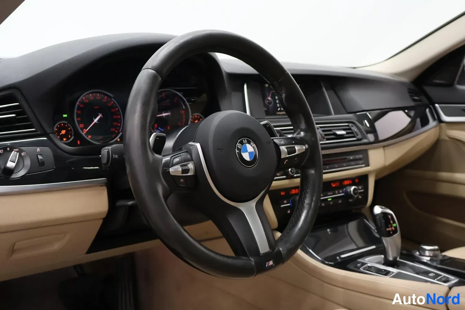 Muu: BMW:n kuljettajan puolen ohjaamo: musta M-urheiluratti, urheilumittarit, automaattivaihteen valitsin ja beige sisusta.