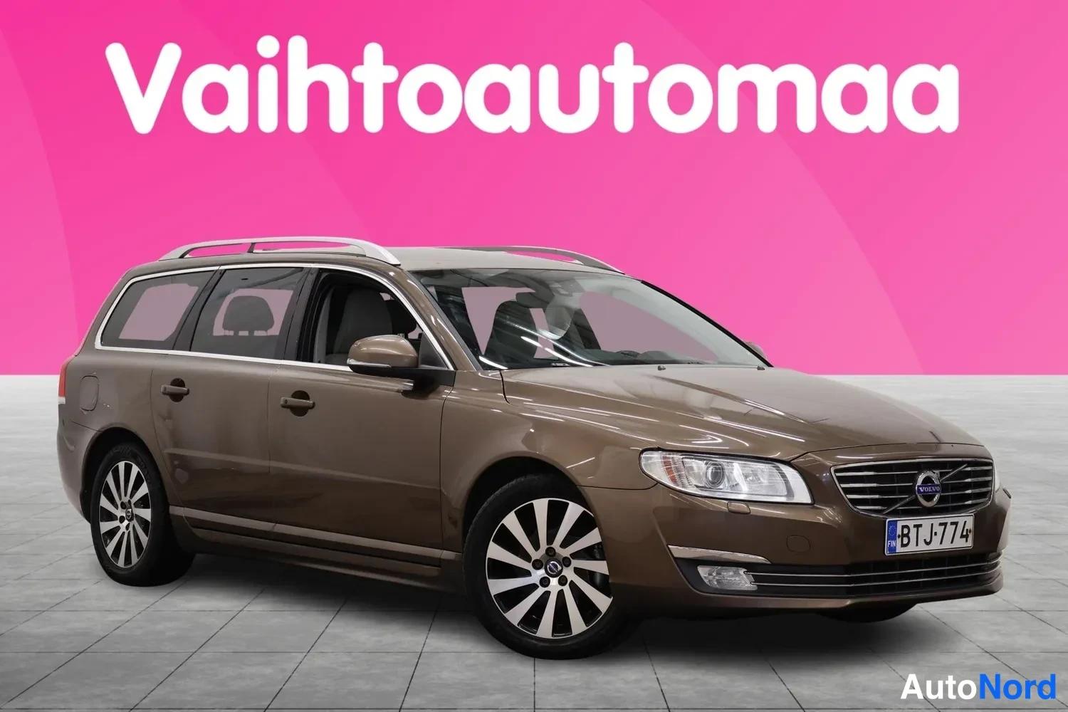 Etuviisto, nokka oikealle: Ruskean Volvo V70 -farmarin etukulma oikealta, rekisteritunnus, kattokaiteet ja monisäterät vanteet näkyvissä.
