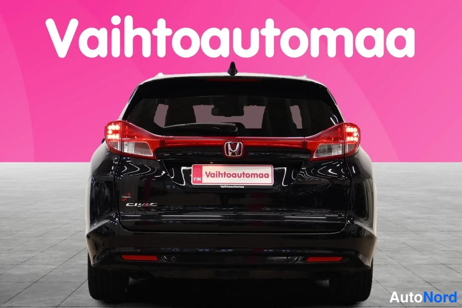 Takaa: Mustan auto takaosa suoraan takaa, punaiset takavalot ja Honda-merkki näkyvät, vaaleanpunaista taustaa vasten.
