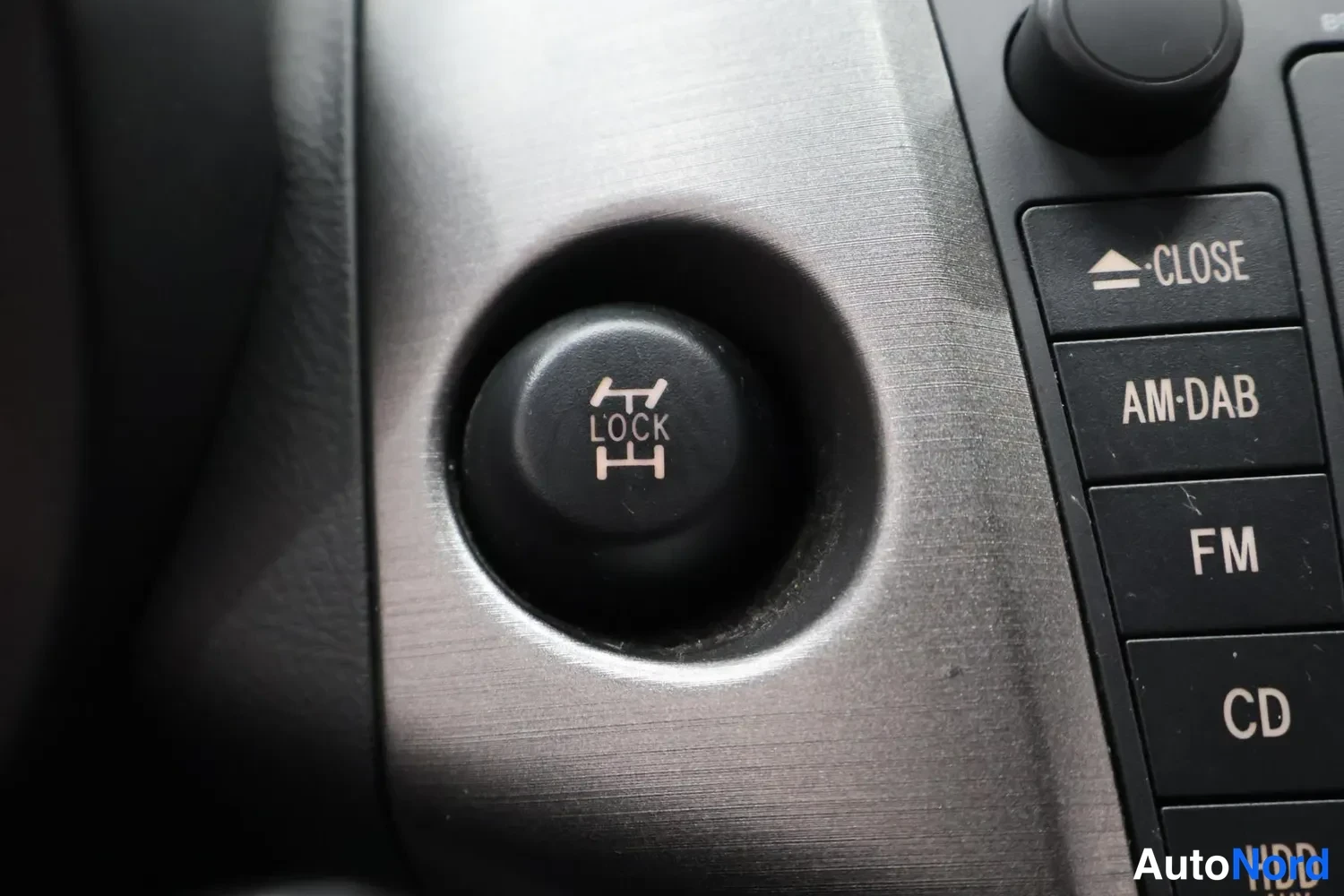 Yksityiskohta: Ohjauspyörän lukitussäädin LOCK ja radion painikkeet CLOSE, AM-DAB, FM, CD ja HDD.