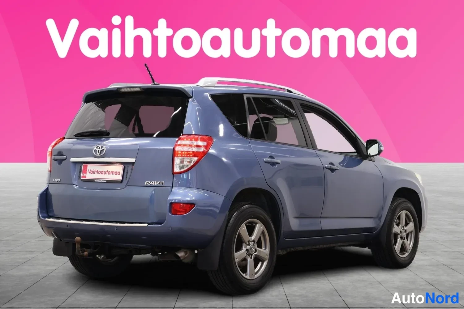 Takaviisto: Sininen Toyota RAV4 takaviistosta vasemmalta nähtynä, sivuovet ja takapää näkyvät.