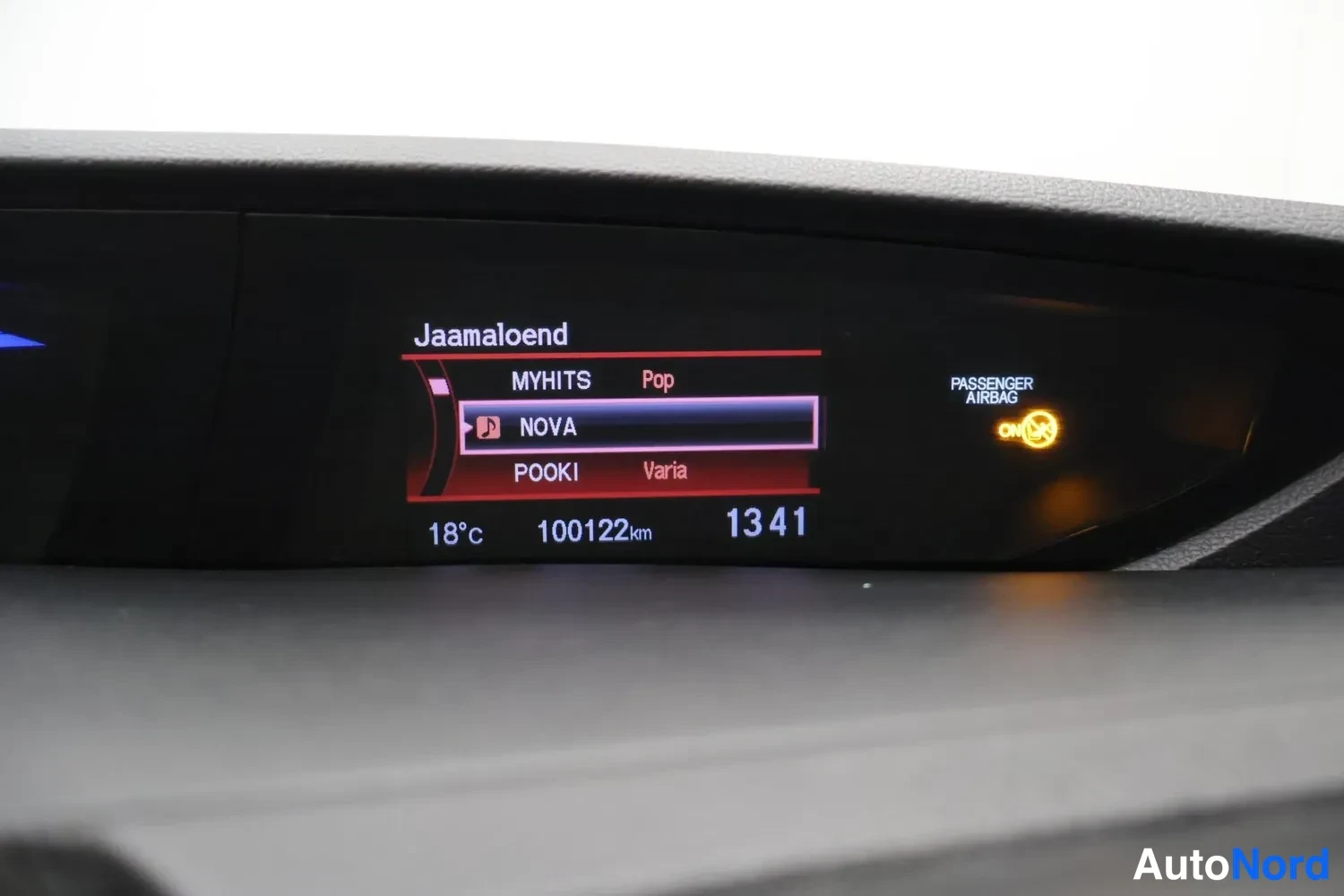 Muu: Kojelaudan infonäyttö radiotiedoilla, matkamittari 100122 km, kello 1341 ja matkustajan turvatyynyn merkkivalo.