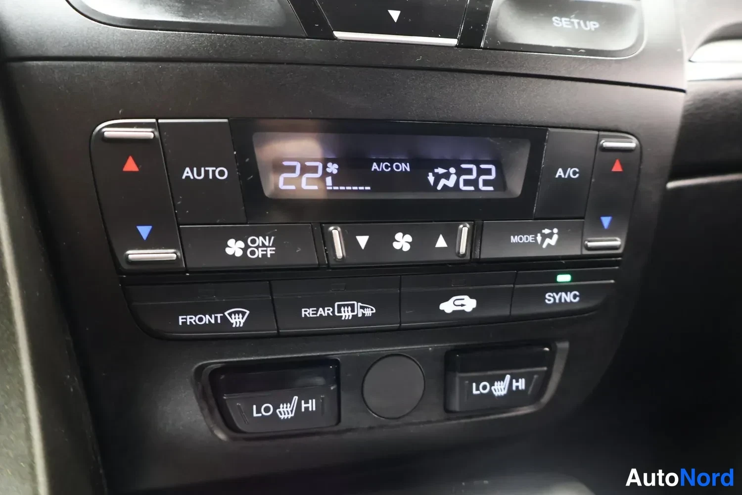 Yksityiskohta: Auton ilmastoinnin ohjauspaneeli: näytössä lukee 22 astetta ja teksti 'A/C ON', alla painikkeita kuten AUTO, A/C, FRONT, REAR ja SYNC sekä kaksi LO–HI-kytkintä